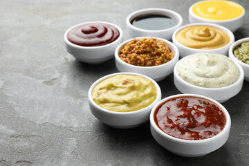 Many different sauces in bowls on grey table, closeup. Space for text