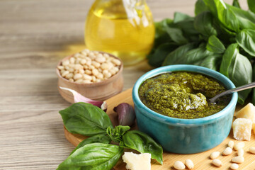Tasty pesto sauce in bowl, basil, pine nuts, cheese and garlic on wooden table