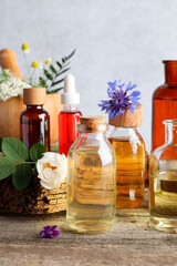 Aromatherapy. Different essential oils, flowers and green leaves on wooden table