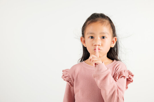 Young kid girl making finger on lips mouth silent quiet gesture, Happy Asian kindergarten child marking silence for stop quiet, mute studio shot isolated on white background with copy space