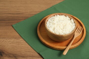 Delicious boiled rice in bowl and fork on wooden table