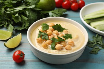 Tasty hummus with chickpeas in bowl and fresh products on light blue wooden table, closeup