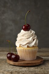 Delicious cupcake with cream and cherries on wooden table, closeup