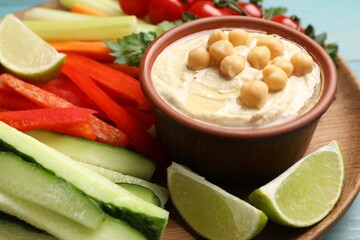 Tasty homemade hummus and different vegetables served on light blue wooden table, closeup