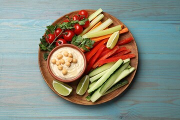 Tasty homemade hummus and different vegetables served on light blue wooden table, top view