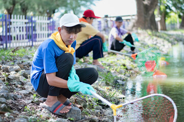 Group of young asian volunteers doing the voluntary work during their weekend by picking and cleaning up plastic bottles from the pond in their community park, soft focus.