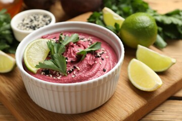 Tasty beet hummus with lime and parsley in bowl on wooden table, closeup