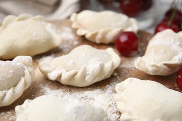 Raw dumplings (varenyky) and fresh cherries on table, closeup