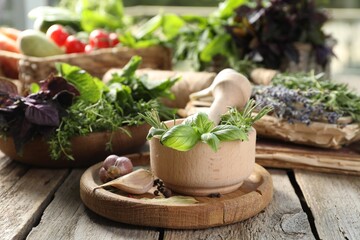 Different aromatic herbs, mortar with pestle and spices on wooden table, closeup