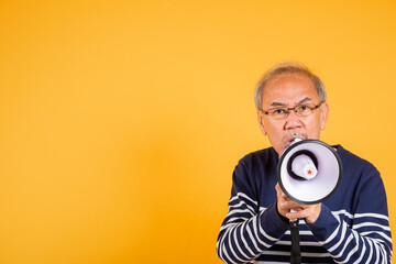 Portrait Asian old man wearing glasses screaming in megaphone studio shot isolated yellow background, happy elderly man holding a megaphone and shouts yelling announces news information