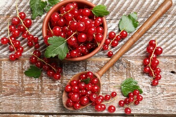 Fresh red currants and green leaves on wooden table, flat lay