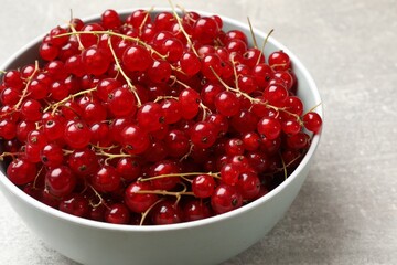 Fresh red currants in bowl on light grey table, closeup