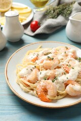Tasty pasta with shrimps, creamy sauce and cheese on light blue wooden table, closeup