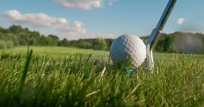 Golf club hits a golf ball in a super slow motion. Drops of morning dew and grass particles rise into the air after the impact.