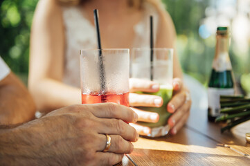 Couple drinking cocktail with slice of orange. Bride and groom holding cocktails. Honeymoon concept after wedding.