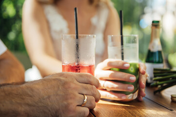 Couple drinking cocktail with slice of orange. Bride and groom holding cocktails. Honeymoon concept after wedding.