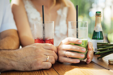 Couple drinking cocktail with slice of orange. Bride and groom holding cocktails. Honeymoon concept after wedding.