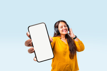 Indian asian Female showcasing smartphone with empty screen, listening to music with headphone .
