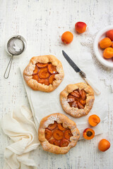 Apricot galette. Homemade three small apricot pie with fresh apricot served for summer tea party on old wooden light table background. Traditional family recipe. Top view with copy space.