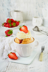 Strawberry banana mug cake. Fresh homemade cake in mug with strawberry, banana and whipped cream in white rustic ceramic mug cup on white wooden table background. Healthy breakfast cooked in microwave