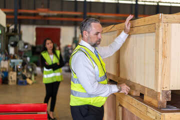Professional senior man worker inspecting a large wooden crate in a warehouse, industrial...