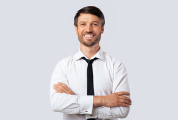 Cheerful Business Guy Smiling At Camera Crossing Hands Standing Over White Studio Background. Isolated, Empty Space
