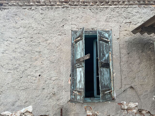 Old Mediterranean house exterior wall, with broken wooden window. Abandoned building with cracked facade, old crumbling plaster exposing bricks. Athens, Greece.