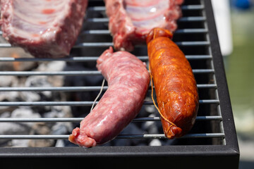 Image of raw pork ribs spread out on a grill, above glowing charcoal, set against an outdoor backdrop illustrating preparation of a traditional barbecue meal.
