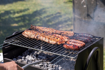 This image captures a barbecue scene with raw ribs and sausages being grilled over a charcoal fire, representing a typical outdoor cooking experience and social gathering activity.