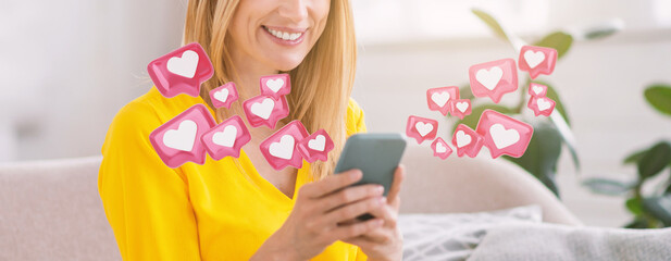 A woman sits in a living room, smiling while looking at her smartphone. Pink hearts with white...