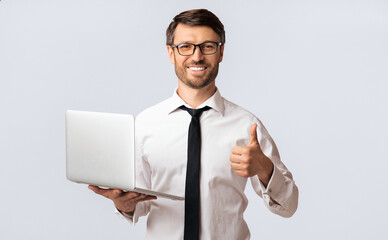 Cool Online Job. Happy Businessman Holding Laptop Gesturing Thumbs-Up Over White Studio Background.