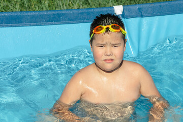 boy, wearing bright orange swimming goggles, stands in the pool, ready to dive in and explore the...