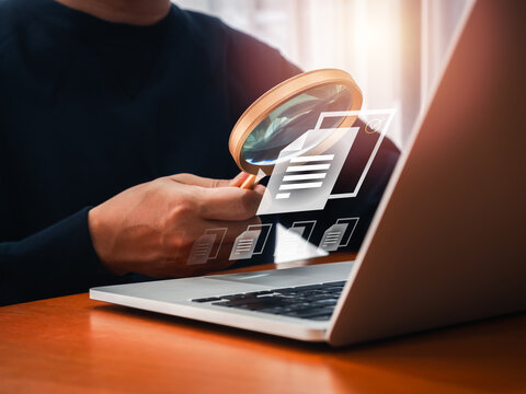 Electronic document check and data information searching online, files manager concept. The right documents file icon appear on magnifying glass in businessman hand while working with laptop computer.