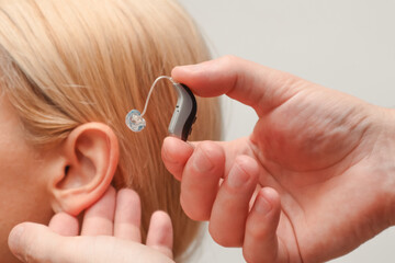 Doctor putting an hearing aid. The hands of a male audiologist trying on a hearing aid on a woman's...