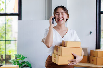 Young asia seller woman happy work on laptop busy cellphone call chat to customer at home office...