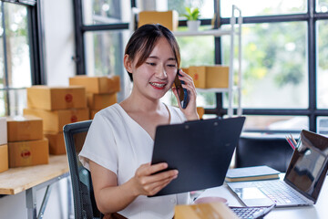 Young asia seller woman happy work on laptop busy cellphone call chat to customer at home office...