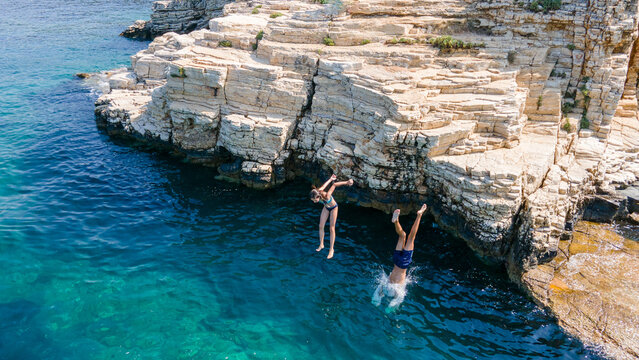 Fun at seaside. Brother and sister jumping from cliff in sea. Girl and boy jumping in sea water at summer holiday. Children jumping off rocks into the sea.