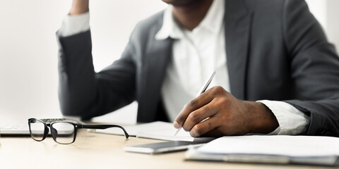 A businessman sits at a desk, writing with a pen on a document.