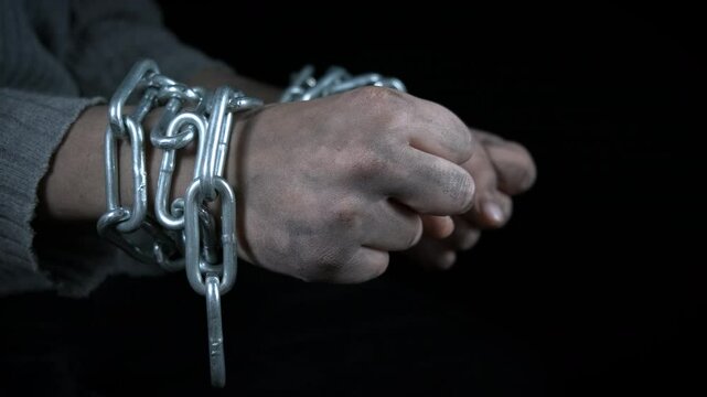 Kidnapping. Dirty hands of a child are chained on a black background.