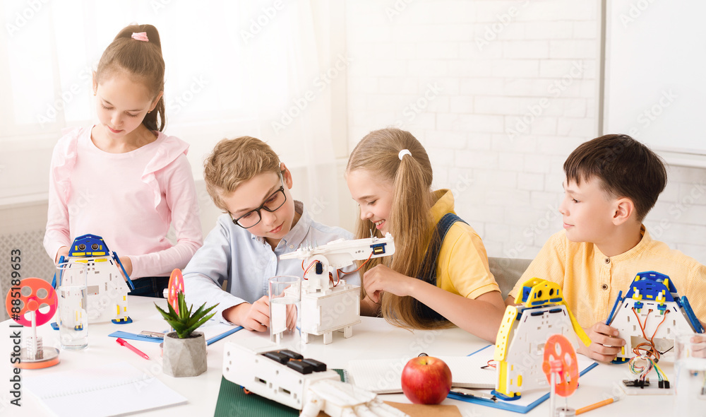 Poster Four children, three boys and one girl, are working on building robots in a classroom setting. They are all focused on their tasks and seem to be enjoying themselves. The classroom is bright
