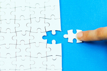 A person is trying to solve a jigsaw puzzle with a hand on a piece