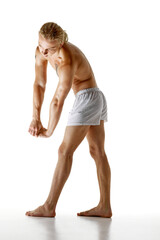 Naklejka premium Shirtless man with long blonde hair, wearing white boxer panties, clasping his hands together, showcasing his muscular arms and torso in stretching pose. Concept of natural beauty and health. Ad