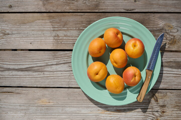 Fresh apricots on turquoise plate with knife on rustic wooden table