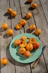 Whole and halved apricots on turquoise plate with knife on rustic wooden table