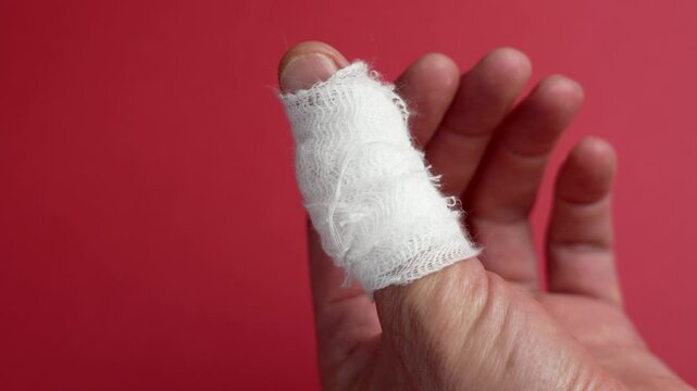 Injured thumb bandaged with a white medical bandage on a bright red background symbolizing pain and injury. Close up