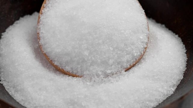 White magnesium salt for relaxing spa in dark bowl with wooden spoon. Rotation. Body care ingredient