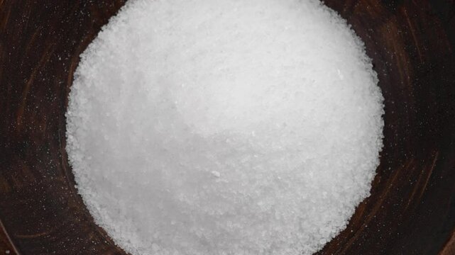 Mound of white sea salt filling a rustic wooden bowl top view close up. Rotation