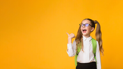 Look There. Excited Elementary Student Girl Pointing Thumb At Free Space Over Yellow Background In Studio. Panorama