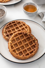 Homemade oatmeal and chia seed waffles on a white plate, accompanied by honey and ingredients