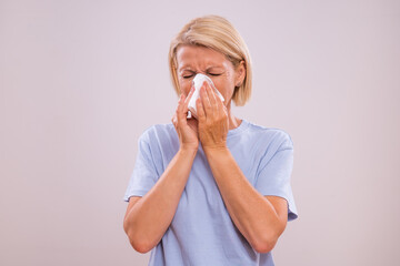 Mature woman is having flu and sneezing into handkerchief.